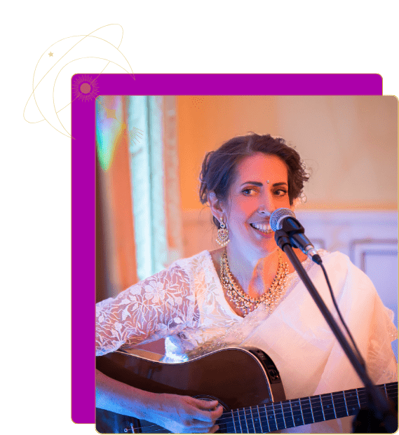 ShantiMaa im Glitzerpullover und rosa Schal, lächelnd an einen Baum gelehnt